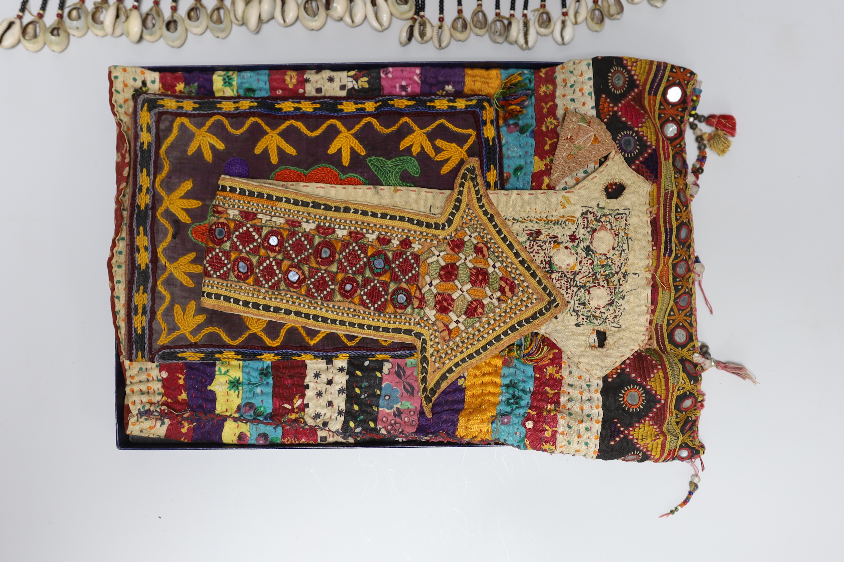 19th and 20th century textiles: An Indian mirrored and patchwork bag, a smaller embroidered bag, an ‘arrow’ shaped mirrored panel and two Omani shell and beaded ‘anchor’ shaped hangings, ‘arrow’ hanging 45cm long (5)